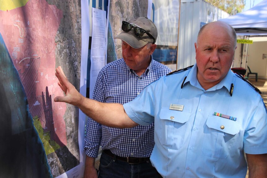 Two men inspect a map on a wall showing the extent of a fire ground