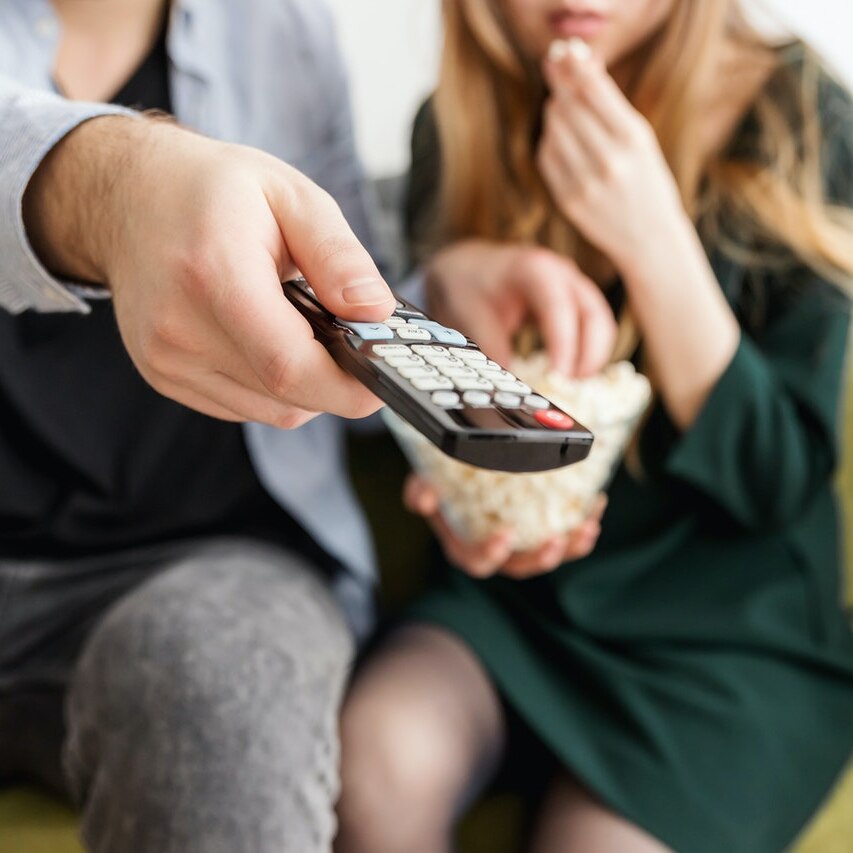 A close up of a couple watching TV, a man's hand holding a remote control