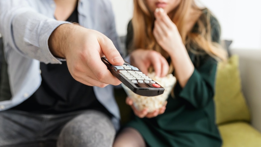 A close up of a couple watching TV, a man's hand holding a remote control