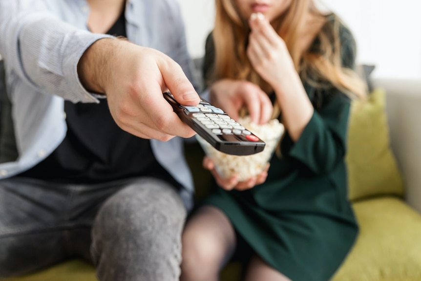 A close up of a couple watching TV, a man's hand holding a remote control