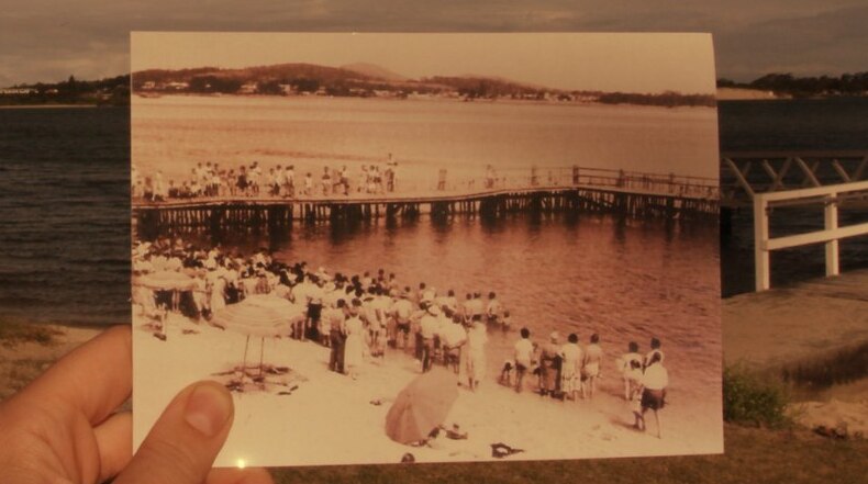 An old photo of the Tuncurry baths features a large crowd enjoying the water.