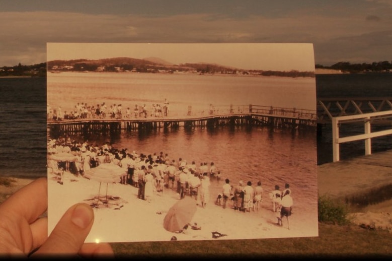 An old photo of the Tuncurry baths features a large crowd enjoying the water.