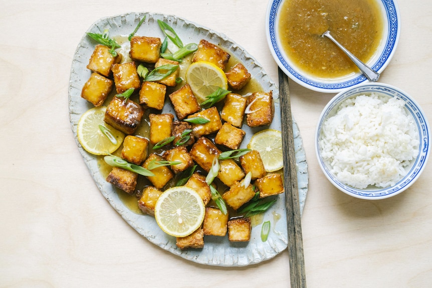 A serving plate of lemon tofu alongside a bowl of rice and sauce, a vegetarian dinner by Hetty McKinnon. 