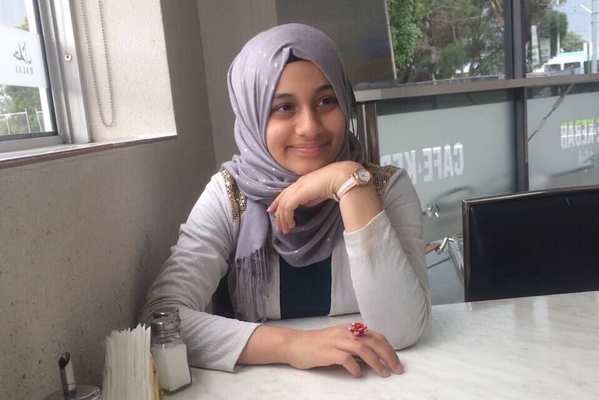 Melbourne girl Zynab Al Harbiya sits at a cafe and smiles at the camera.
