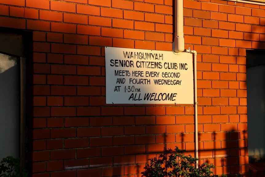 A white sign on a brick wall dappled in early morning sun that reads Wahgunyah senior citizens club inc and All welcome