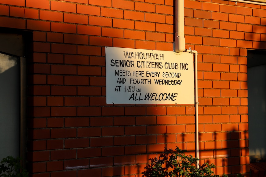 A white sign on a brick wall dappled in early morning sun that reads Wahgunyah senior citizens club inc and All welcome