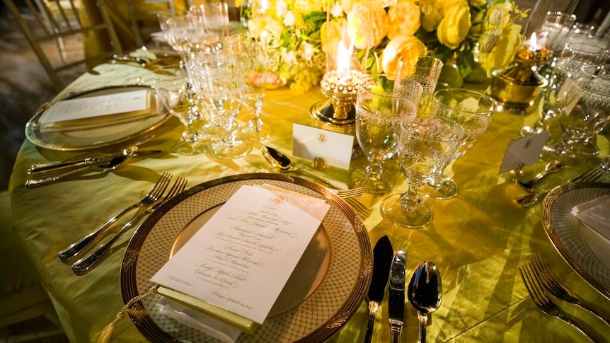 An lavish gold table setting with yellow roses and wattle as the centre piece.