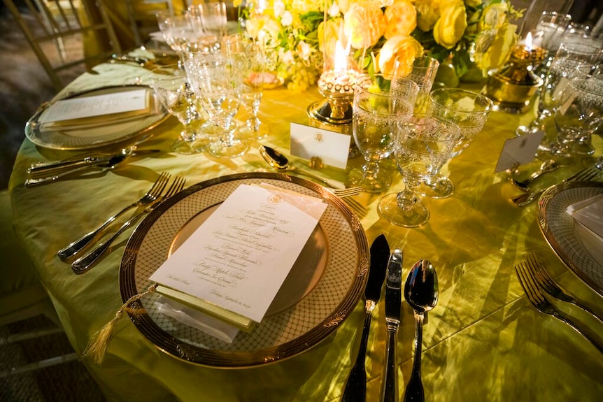 An lavish gold table setting with yellow roses and wattle as the centre piece.