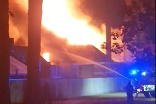 Un pompier tire de l'eau d'un tuyau sur un incendie de structure qui fait rage