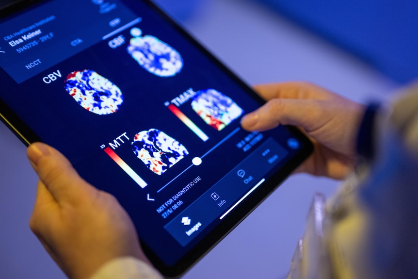A tablet showing brain scans in various colours is held by two hands