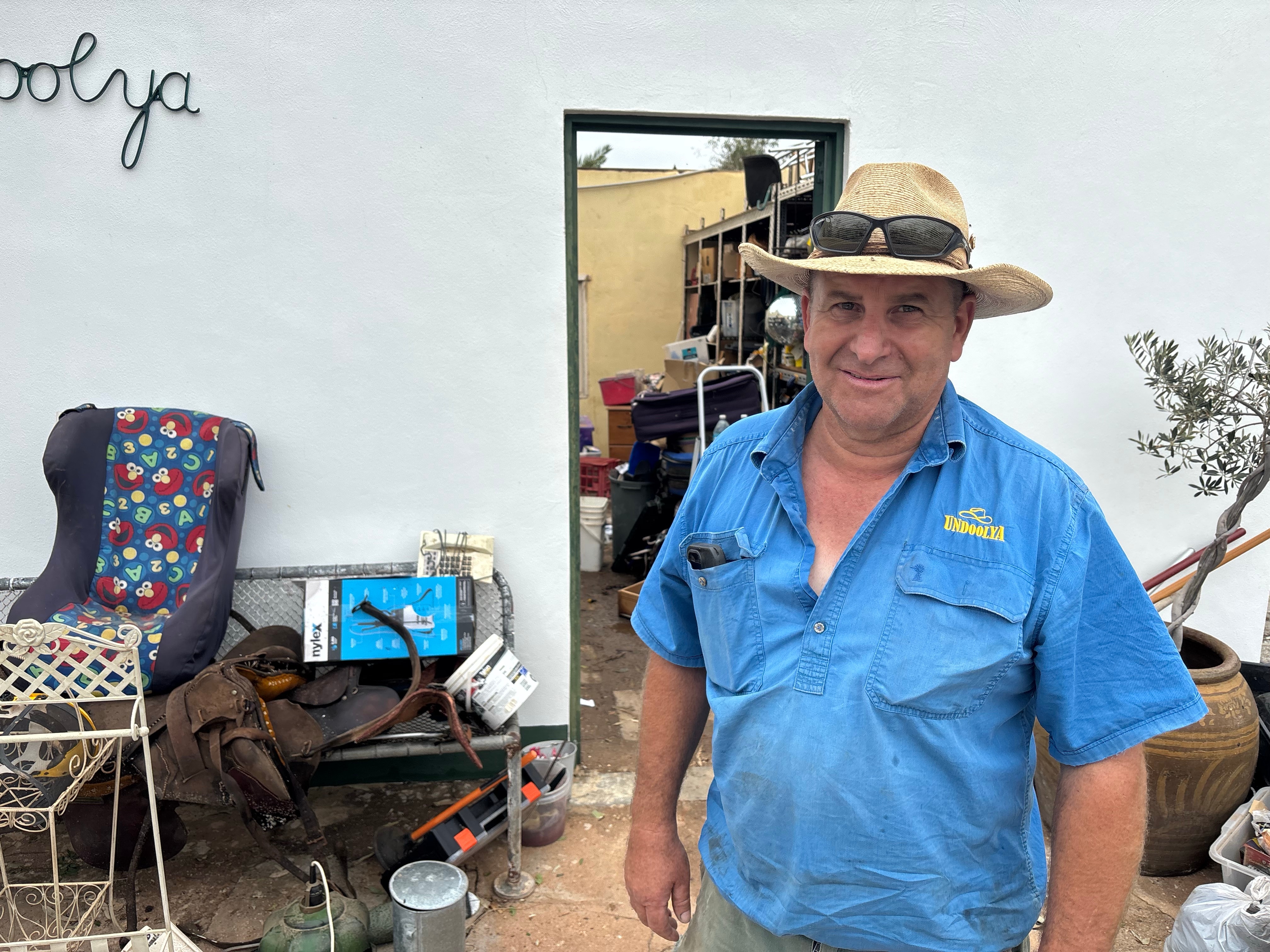 A man in a workshirt and cowboy hat looks at the camera at a cattle station