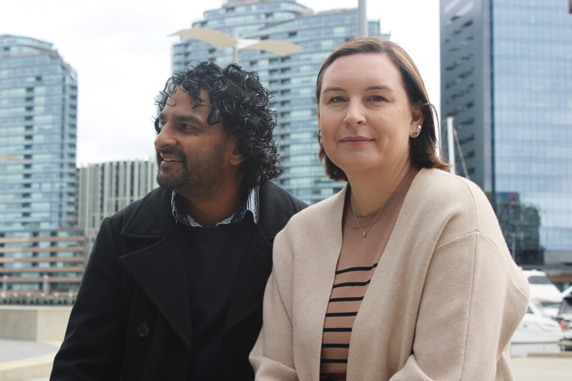 A man and a woman sit together - he looks to the side, she looks to the camera