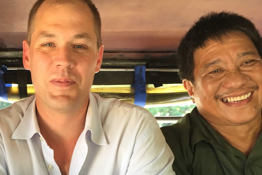 Three men sit in a car facing the camera.