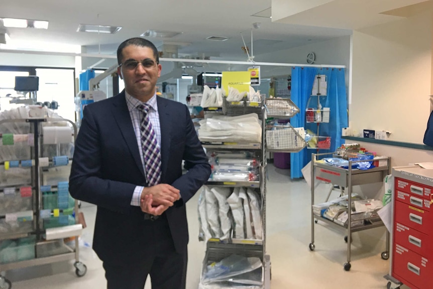 Dr Haris Haqqani stands in a hospital room wearing a suit.