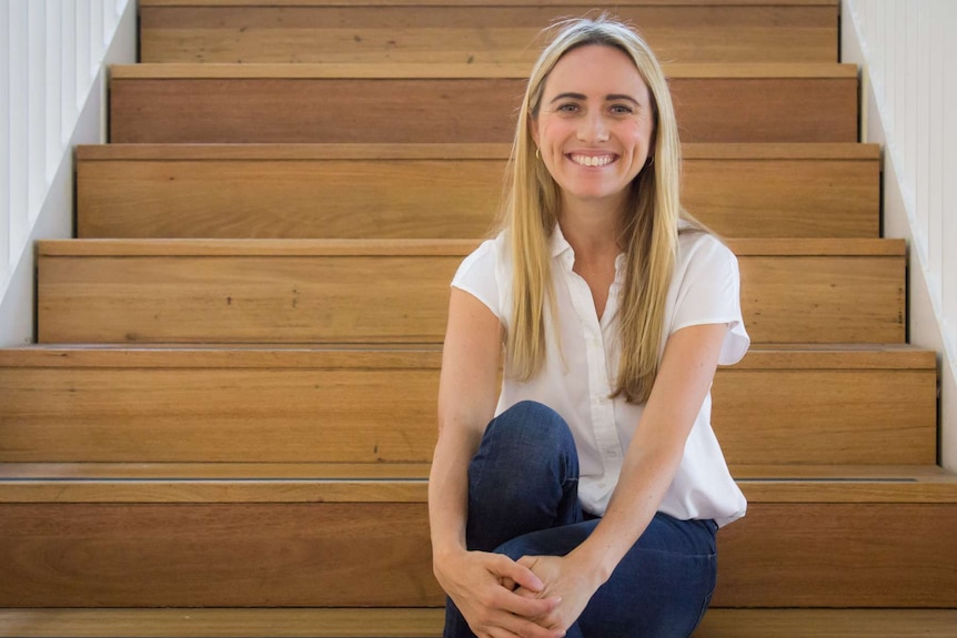 Lady sitting on wooden stairs in white shirt and denim jeans.