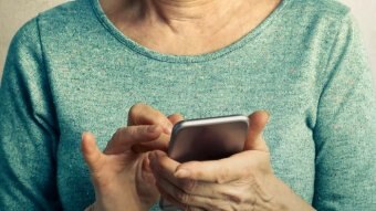 A woman in a green shirt, her face not visible, operating a mobile phone.