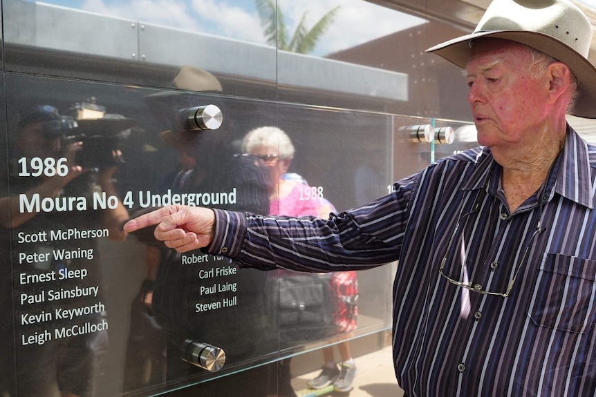 A man points at a list of names on a wall at a memorial for victims in mining disasters.