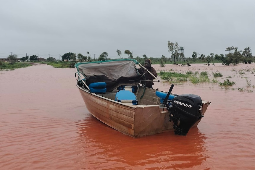 an aboriginal man tending to a dinghy in orange floodwaters in a remote community
