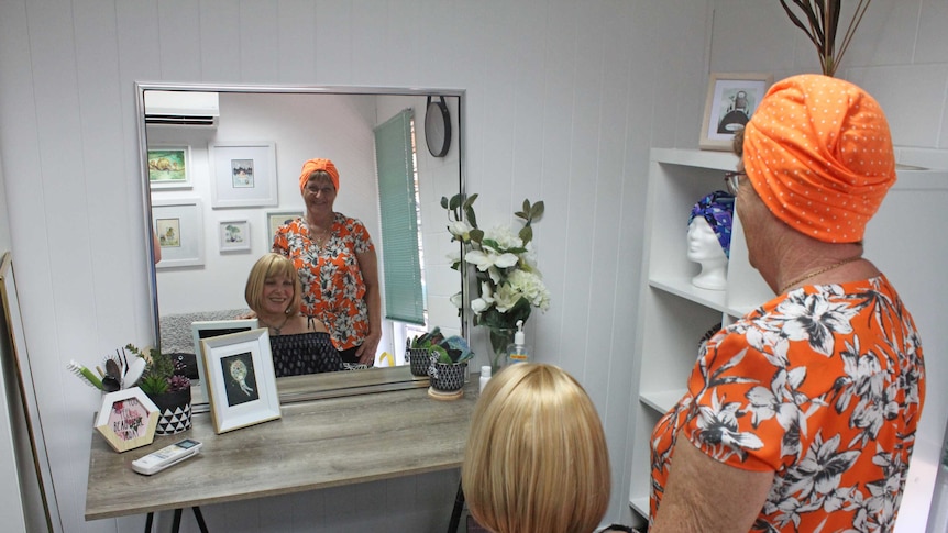 Lady with a blonde bob and another lady wearing a bright orange turban smiling while looking in the mirror.
