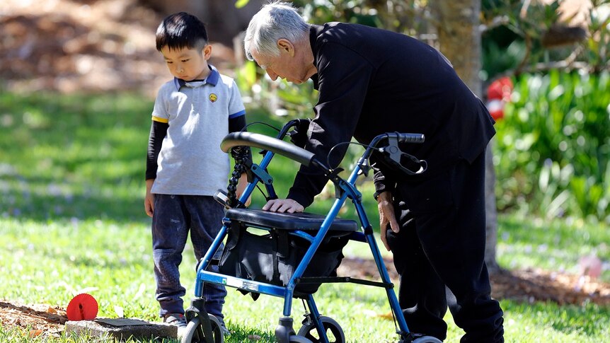 A young child stands next to an elderly man holding onto a walker on the ABC TV series Old People's Home For 4 Year Olds.