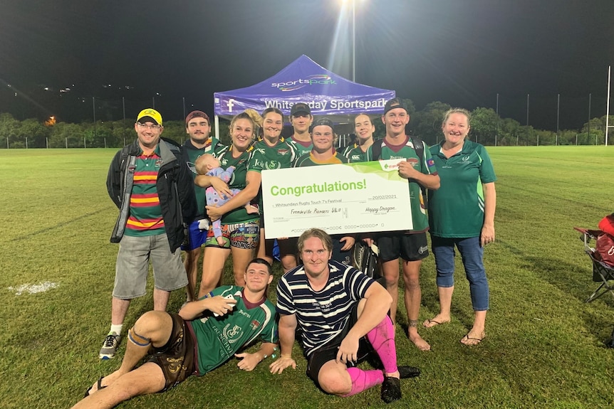 Football team group photo holding large check in front of purple tent 