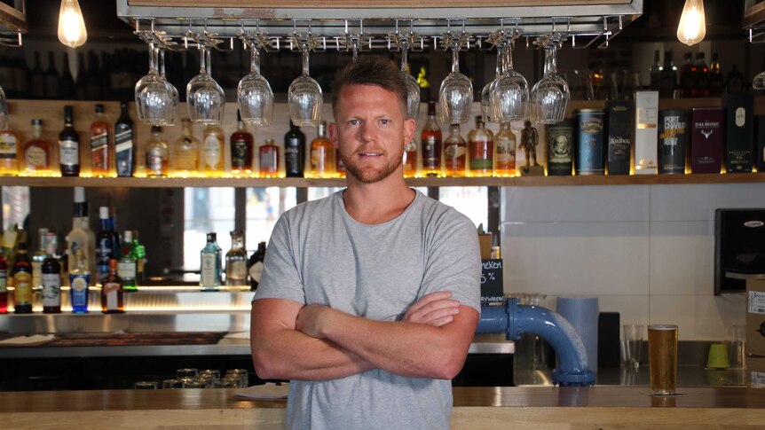 Sandbar owner Ben Randall stands with his arms folded in front of a bar.