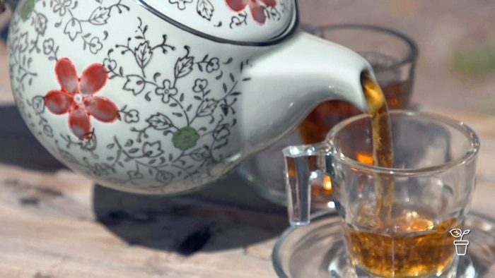 Teapot painted with flowers pouring tea into glass tea cup