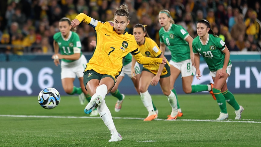 A soccer player wearing yellow and green kicks the ball during a game with opponents wearing green and white behind her