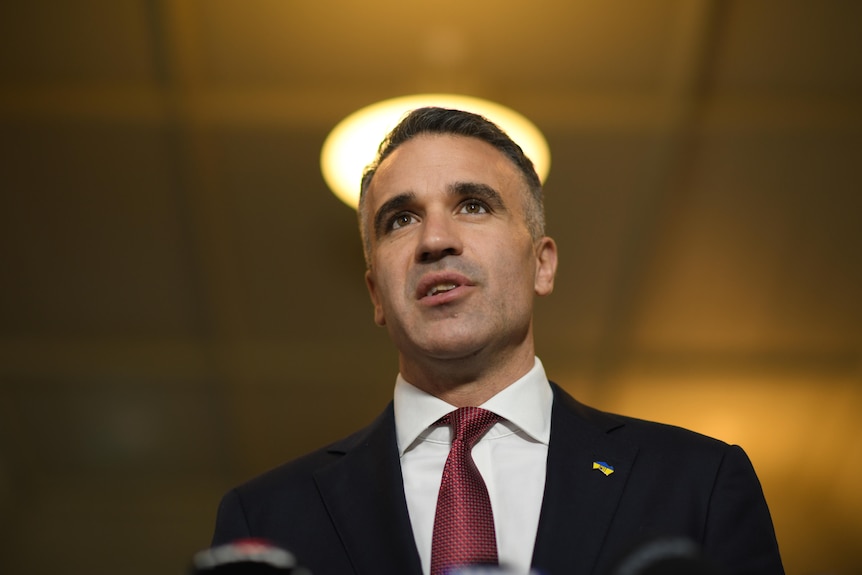 A man in a suit speaking with a round light shining above his head.