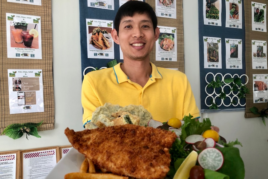 The chef holds up a plate, loaded with fish, tempura vegetables and a vibrant salad.