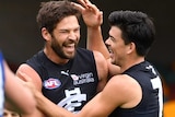 Levi Casboult hugs Matt Kennedy and smiles after kicking a goal. A North player is sad in the foreground