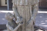 A statue of a saint handing a child bread.