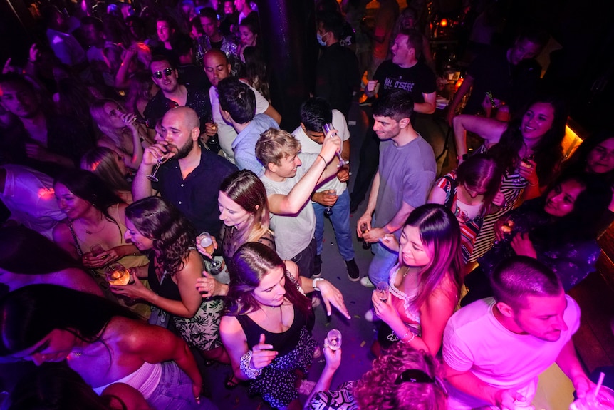 A group of people stand on a dancefloor with their hands in the air