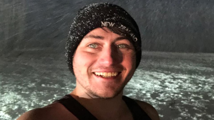 A man wearing a singlet and beanie while snow is falling.