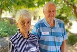 Older couple standing under trees, smiling