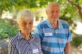 Older couple standing under trees, smiling