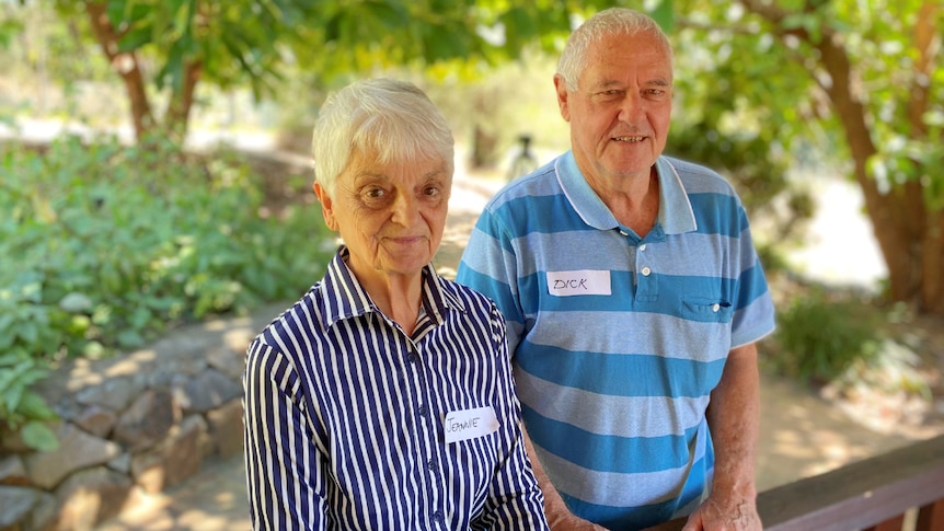 Older couple standing under trees, smiling