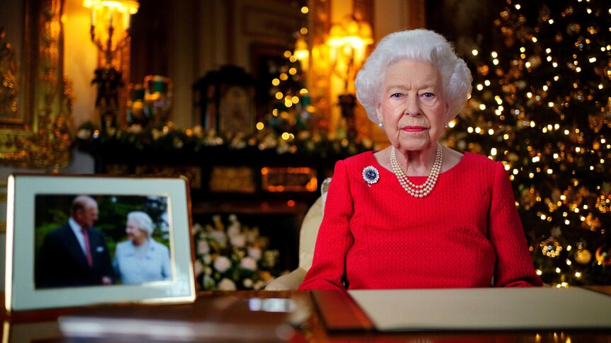 Queen Elizabeth II seated in red dress, photograph with her late husband Prince Philip on the left.