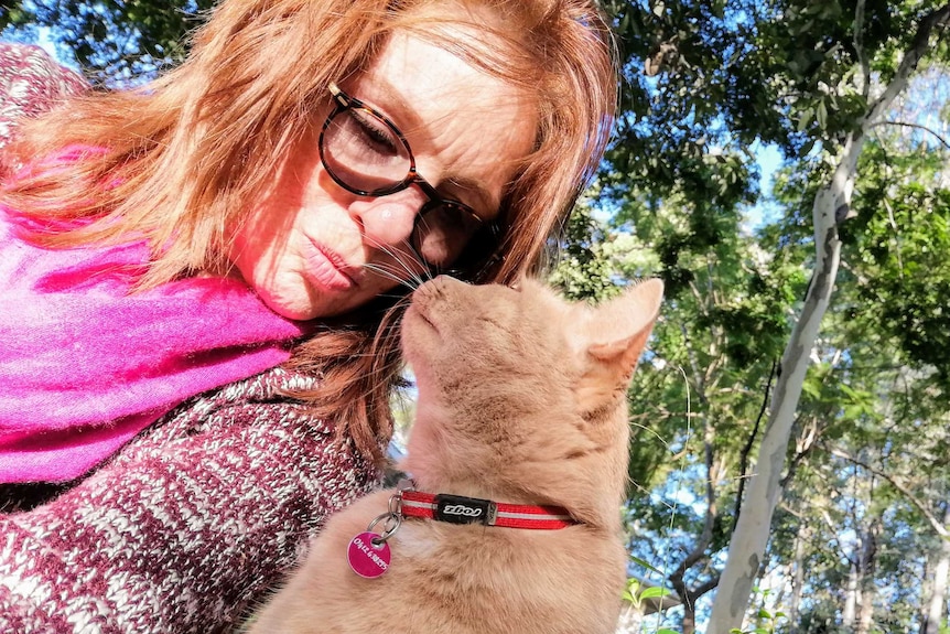 A middle-aged caucasian woman with red hair touches nose with her ginger cat.