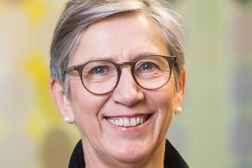 A woman smiling with short grey hair and glasses
