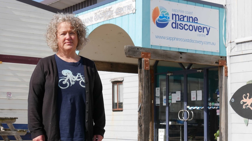 A woman stands in front of the Marine Discovery Centre, wearing a black cardigan