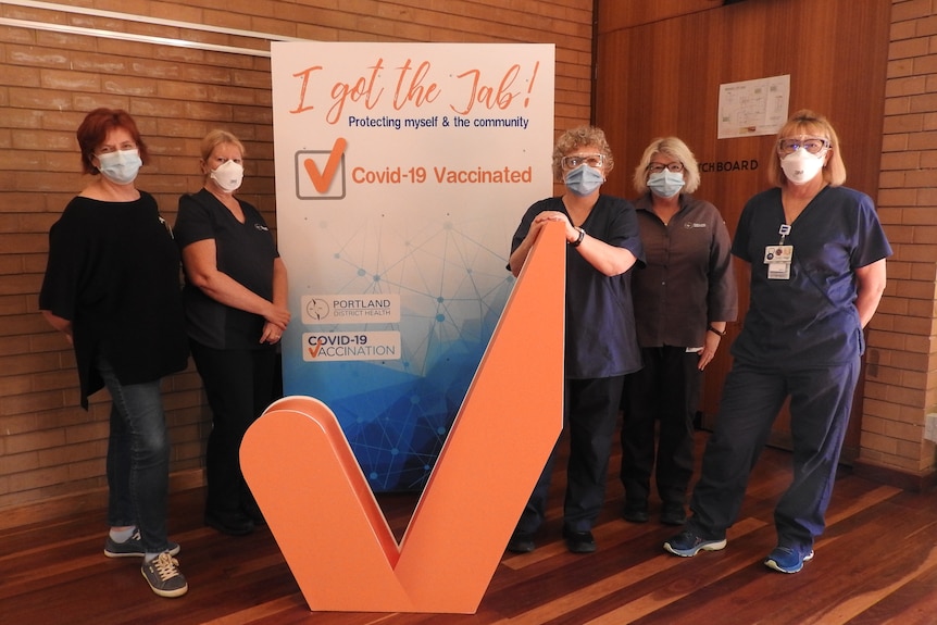 Five healthcare workers in masks standing around vaccination sign