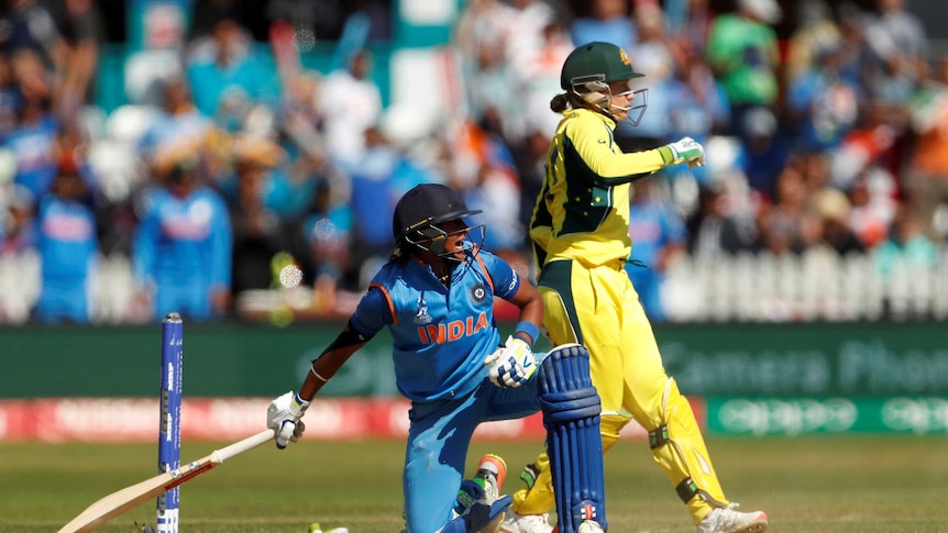 Harmanpreet Kaur, on one knee, looks behind her, while Australia wicketkeeper Alyssa Healy walks past.