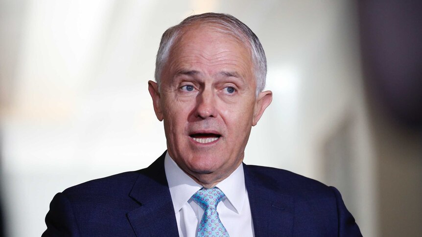 Turnbull is wearing a blue tie and suit. His eyes are looking to the right and his mouth is open.