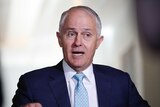 Turnbull is wearing a blue tie and suit. His eyes are looking to the right and his mouth is open.
