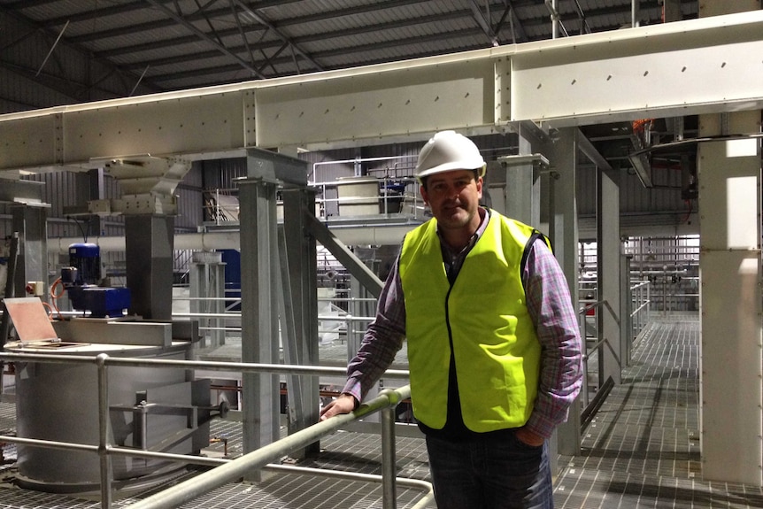 The general manager is surrounded by tanks, pipes and  processing equipment