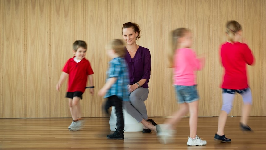 A teacher in the middle of a group of marching children.