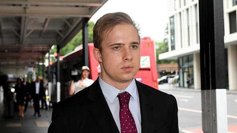 A young man wearing a suit walks along a street.