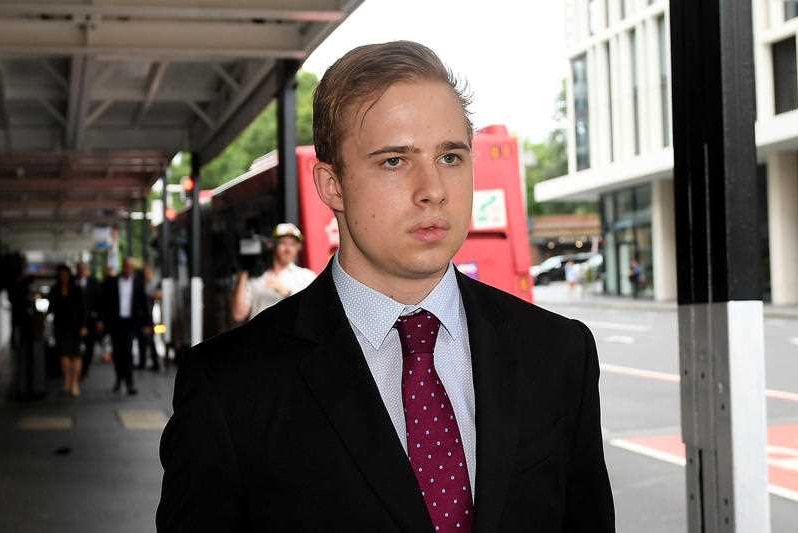 A young man wearing a suit walks along a street.