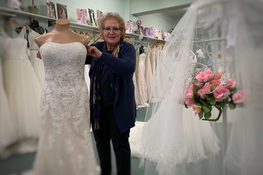An older woman stands in front of a mannequin adjusting a bridal gown